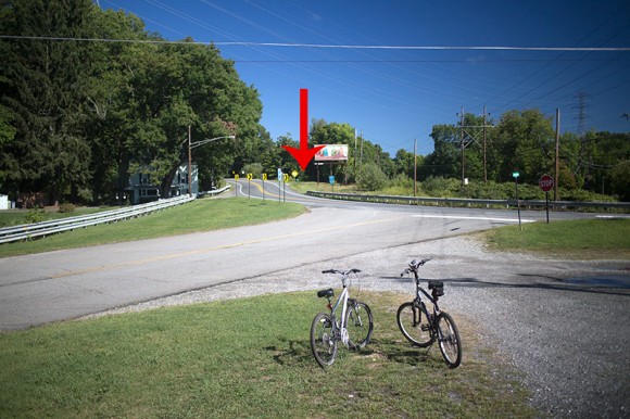 Two bikes at an intersection of several roads with an arrow added to the photo to show where to turn.