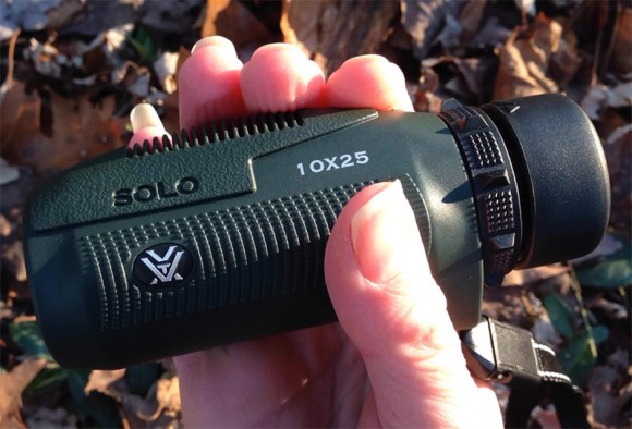 Hand holding a small monocular with leaves in the background.