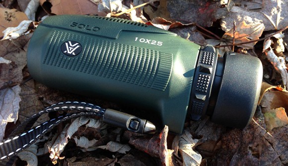 Compact monocular 10x25 power with strap sitting in leaves.