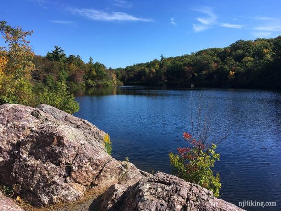 Bright blue pond surrounded by trees with pinkish rocks in the foreground