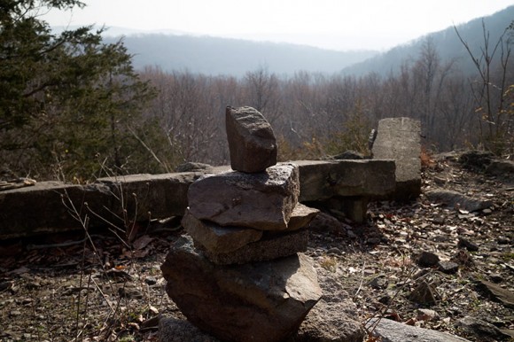 Rocks stacked neer the cement remains of a cabin with mountains in the distance