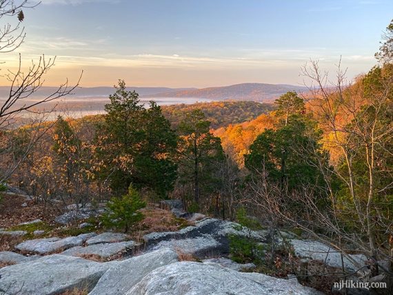 View from the Summit trail of low clouds hanging over fall foliage glowing in early morning sun.