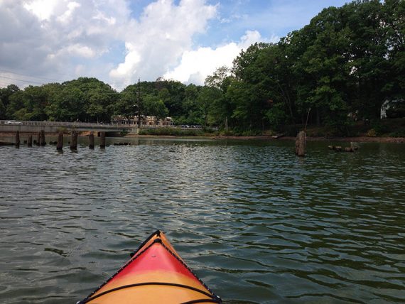 Tip of a kayak in front of wooden pylons in a lake.