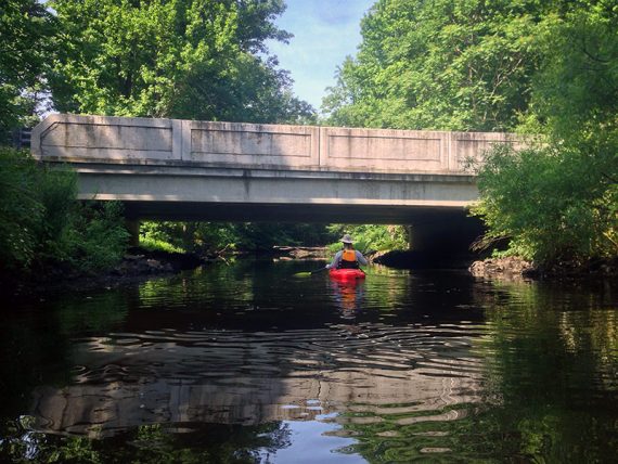 Kayker paddling under a low cement bridge.