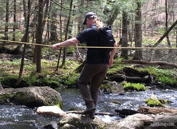 Hiker crossing a stream wearing Konfidant Air pants.