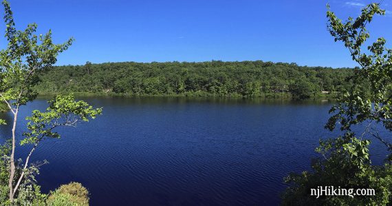 Beyond bright blue Surprise Lake is a hill covered in green trees.