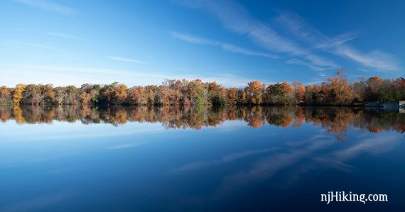 Trees with fall color reflected in a blue lake.
