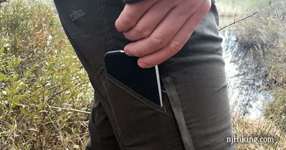 Hiker sliding a cell phone into a thigh pants pocket.