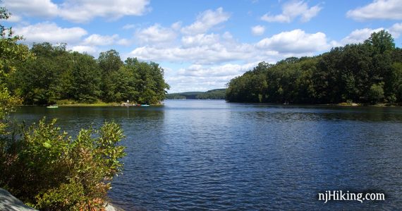 Bright blue lake with green trees on either side and white clouds above.