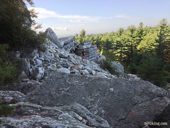 Hiker going over a rocky area near a cliff edge.