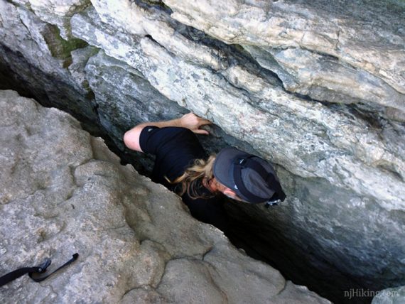 Looking down at a hiker squeezing through a narrow rock crevice.