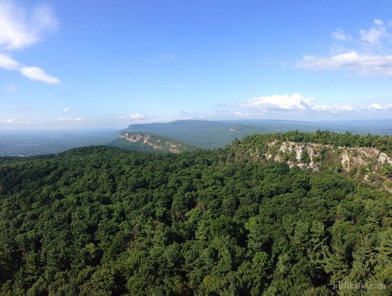 Viewpoint over bright green forest and steep white cliff faces.