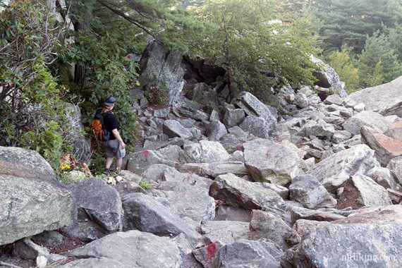 Hiker going downhill over many pointed rock slabs.