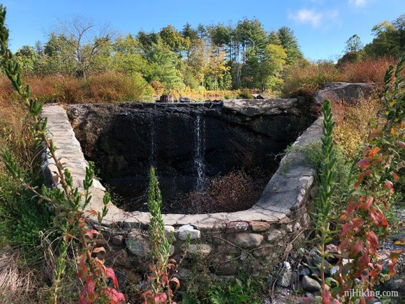 Stone spillway structure at the edge of a manmade pond.