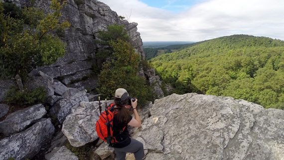 Hiker holding a camera near the edge of a cliff.