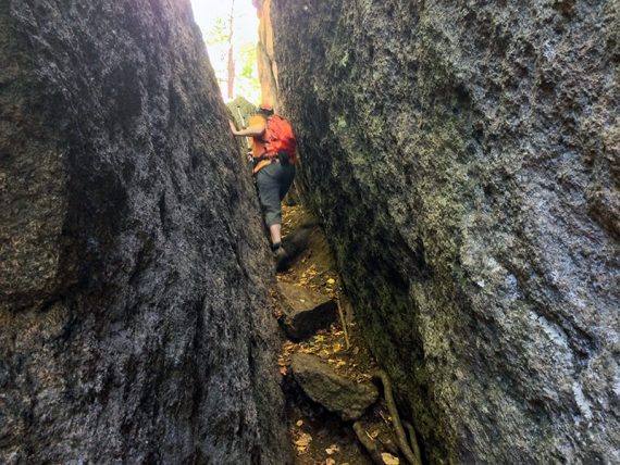 Hiker squeezing between two large slanted rock faces