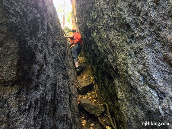 Hiker squeezing between two large slanted rock faces