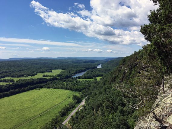 Cliff face with green field below and river in the distance.