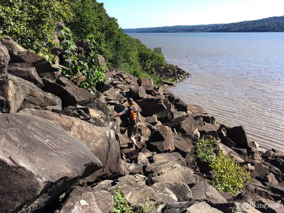 Hiker scrambling over a jumble of rocks by the Hudson River.