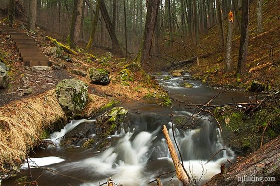 Water cascading over rocks near wooden steps.