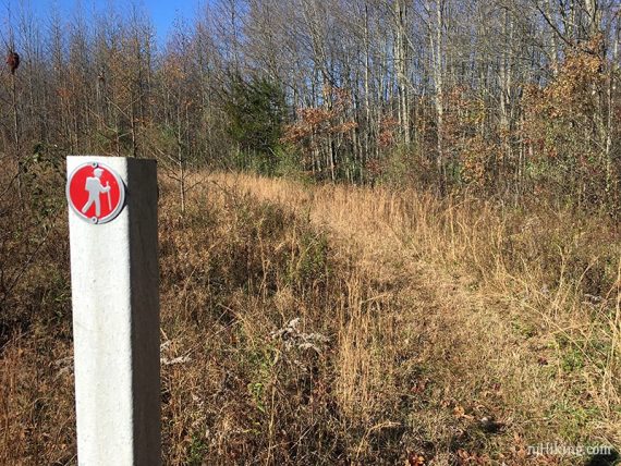 Round red hiker trail marker along a field edge.