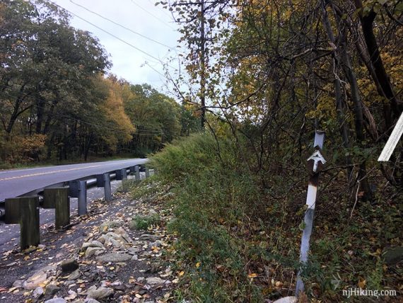 White AT sign on a marker post where the trail goes along a guardrail.