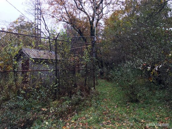 Small utility shack behind a chain link fence.