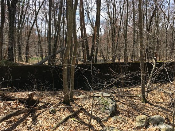 Remains of a dam wall, with a dry pond beyond.