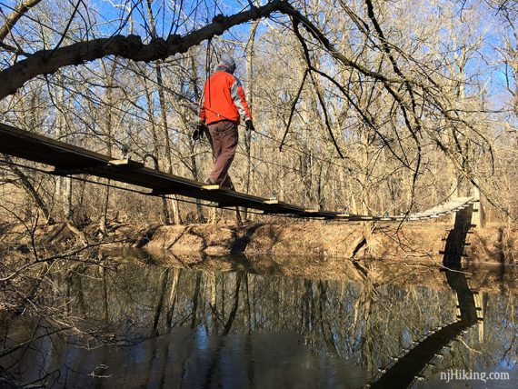 Hiker crossing a swinging bridge over a stream.