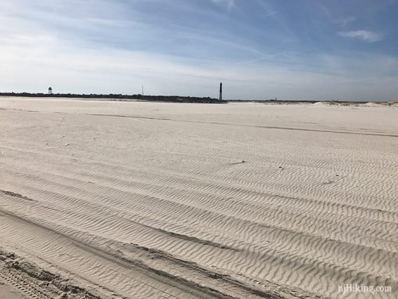 Tire tracks on the beach with a lighthouse in the distance