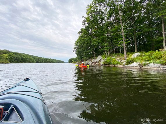 Kayakers along a rocky shoreline ringed with trees.