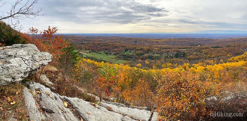 Panoramic view from a rocky ledge over a valley with fall foliage.