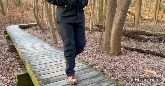 Hiker on a trail boardwalk wearing dark softshell pants.
