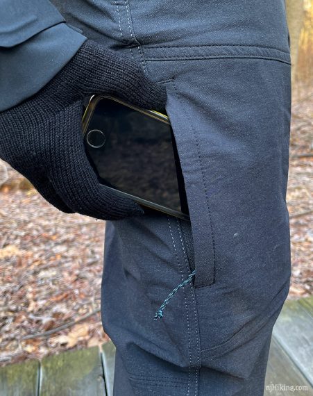 Hiker putting cell phone into a zippered thigh pocket.