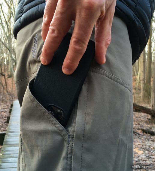 Cell phone being put into a hiking pants pocket.