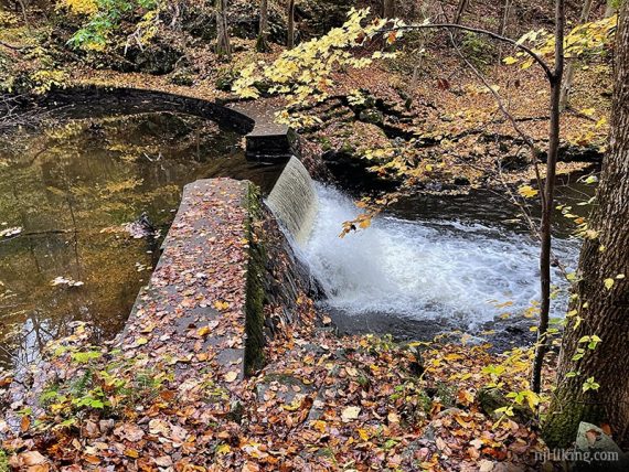 Stone wall and dam with water flowing over it.