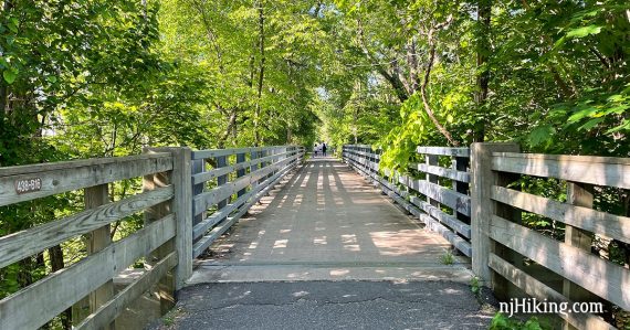 Paved trail with wooden fence and surrounded by trees