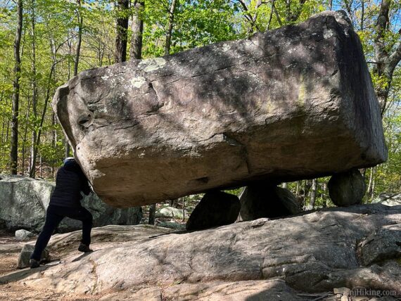 Hiker pushing tripod rock.