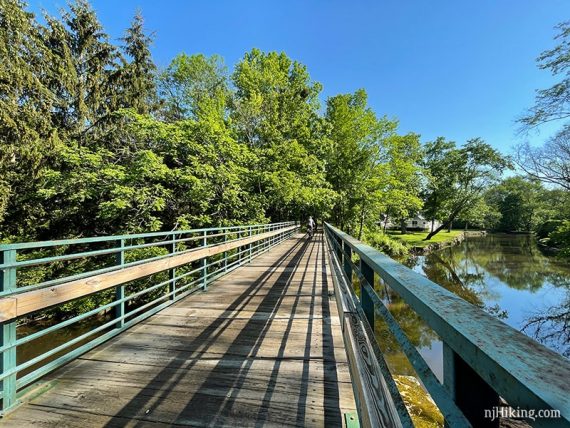 Long wooden bridge over river with bike rider in the distance.