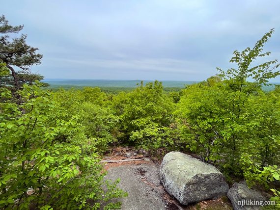 Large rock at a viewpoint with green foliage beyond.