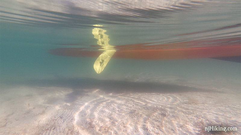Bottom of a kayak and paddle seen through clear water with a white bottom