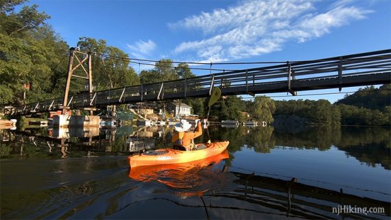 Kayaker paddling under a footbridge