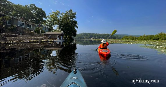 Kayaker paddling near a lakeside house with a mountain in the distance