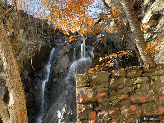 Water cascading down a steep rock face with a stone wall in the foreground.