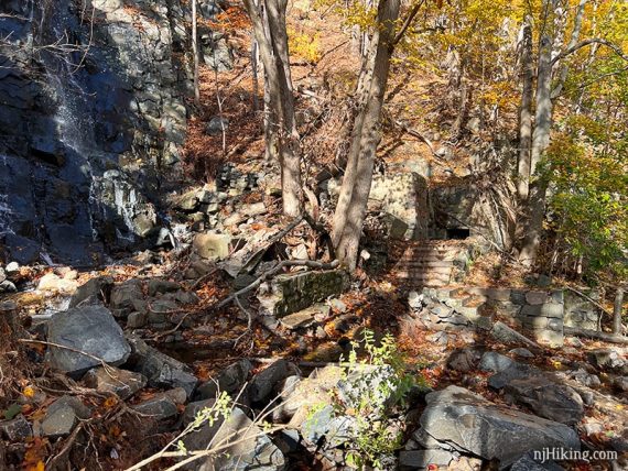 Old stone steps and remains of a building next to a waterfall.