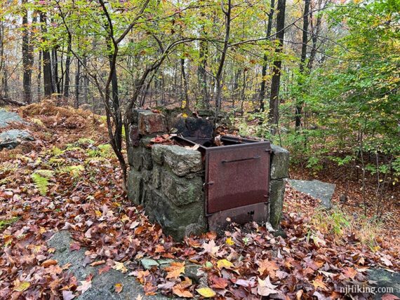 Old stone grill with a rusted door in the middle of the woods