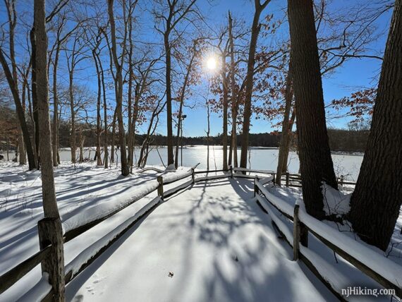 Snow covered fenced path leading to a frozen lake