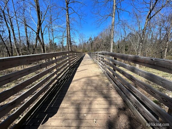 Long wooden bridge with railings over a mostly dry stream.