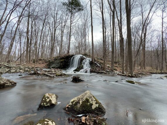 Water cascading over a rocky hill into a brook with large rocks in the foreground