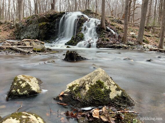 Water cascading over a rocky hill into a brook with large rocks in the foreground.